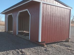 Under a clear blue sky, the Horseman - 2303 stands proudly as a red, open-sided barn structure with a sleek black roof on a gravel surface.
