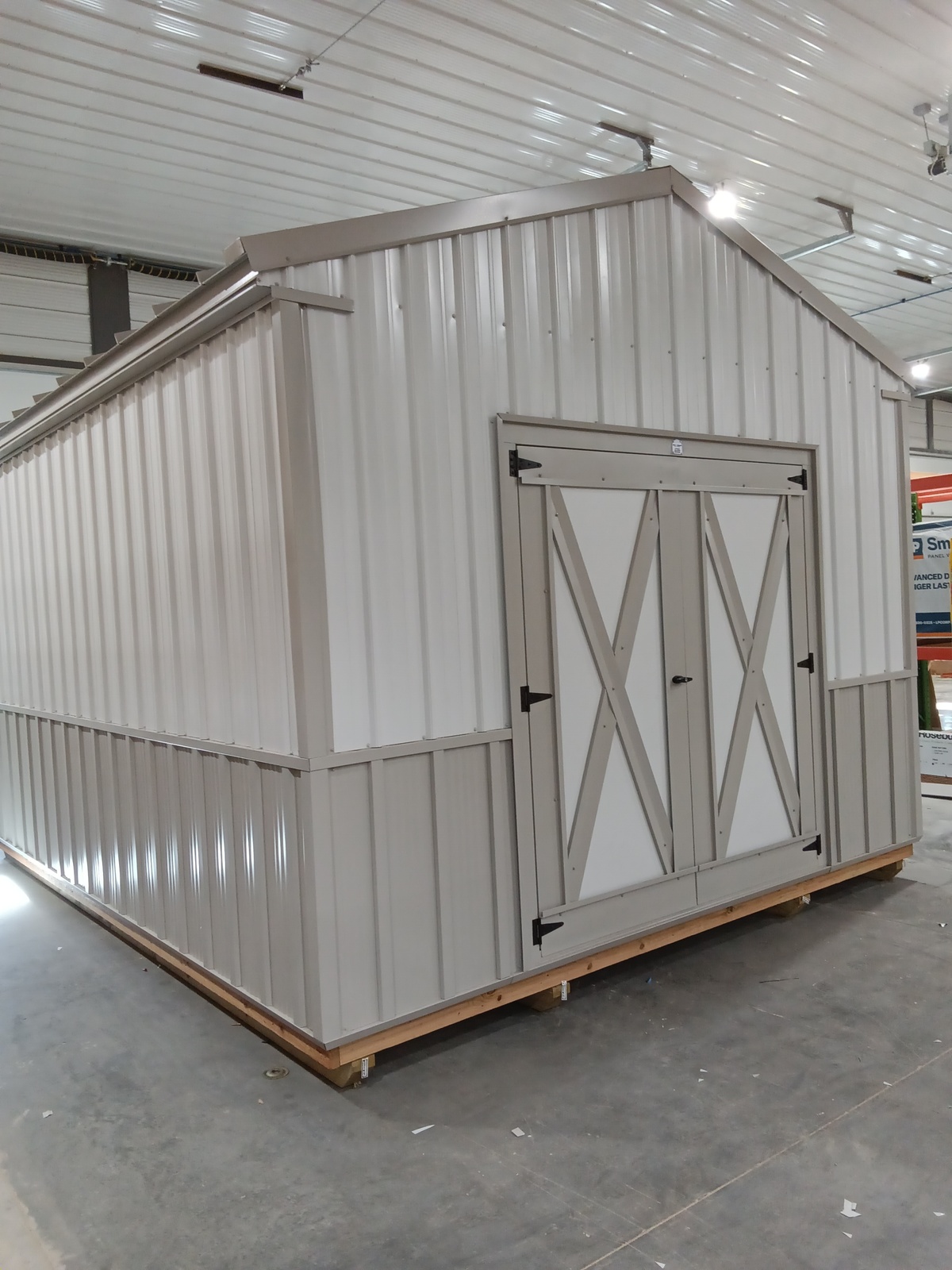 A Classic Shed - 2405 storage shed in light gray and white, featuring double doors, is placed indoors on a concrete floor beneath a white ribbed ceiling.