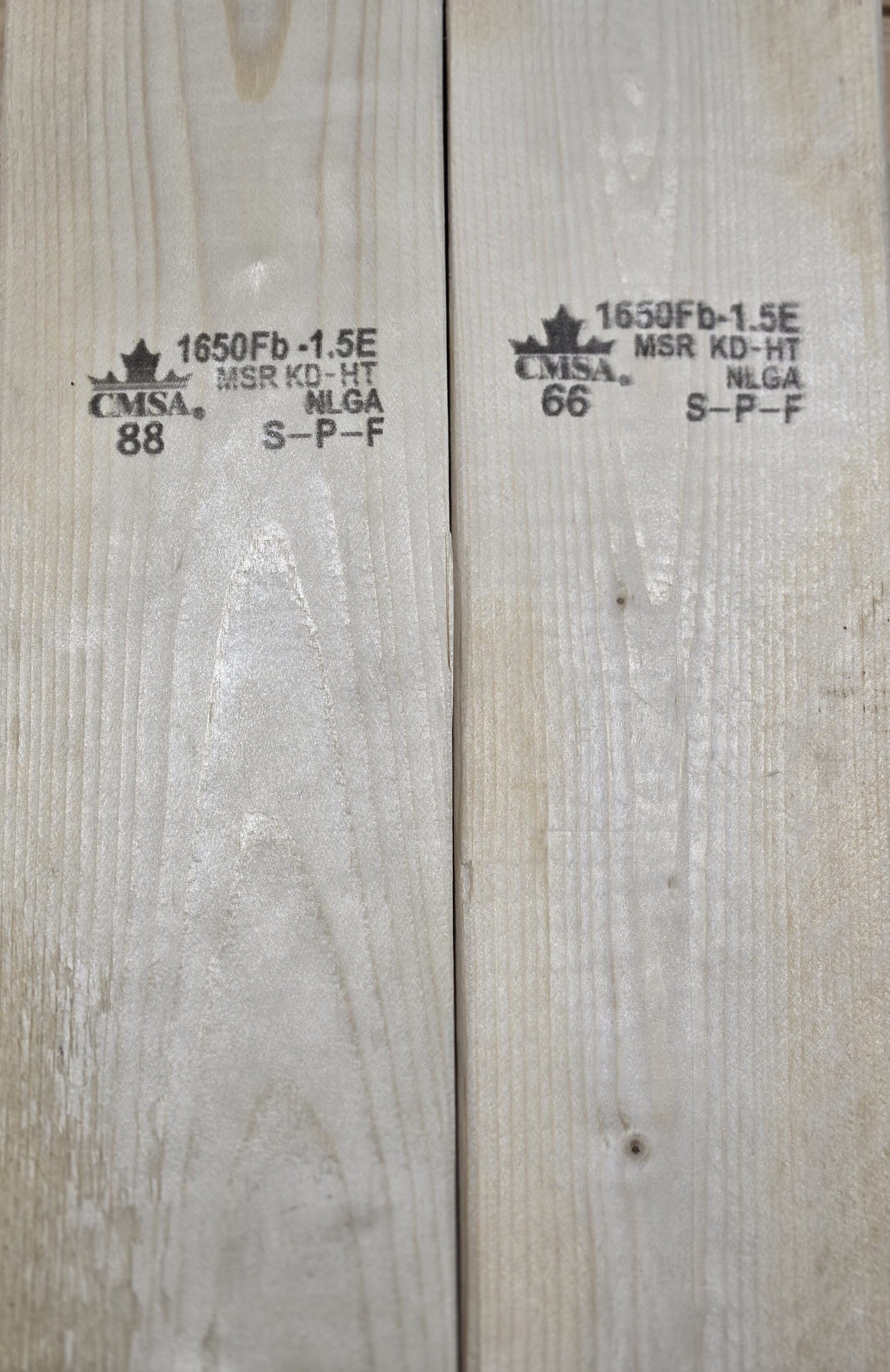Two wooden planks with stamps showing grading information, perfect for constructing Delta Sheds or adding a touch of craftsmanship to your home. Stamps read "CMSA," "1650Fb 1.5E," "MSR KD-HT," "NLGA," and "S-P-F." Numbers "88" and "66" are also visible on the light finish with grain patterns.