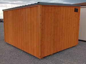 The Lean-To - 2931 is a large wooden storage shed with vertical orange-brown panels and a slanted metal roof, set on gravel beneath a cloudy sky.