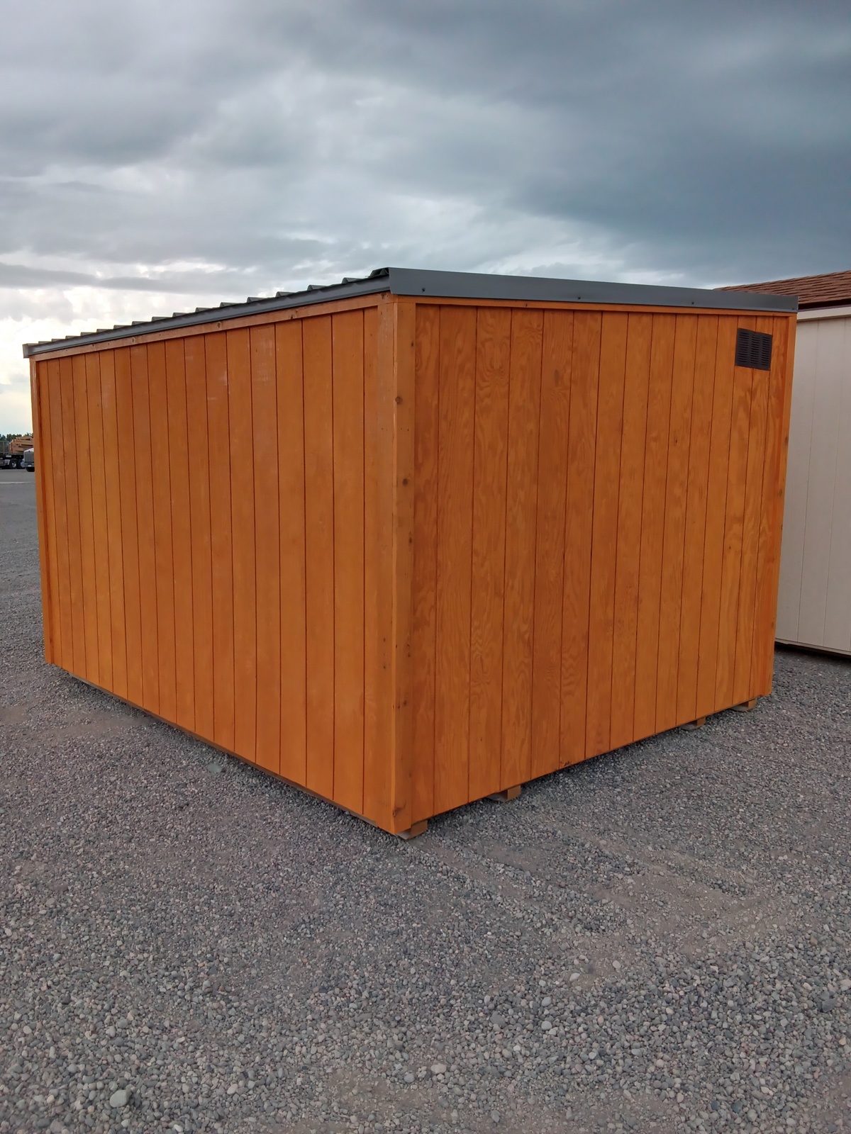 The Lean-To - 2931 is a large wooden storage shed with vertical orange-brown panels and a slanted metal roof, set on gravel beneath a cloudy sky.