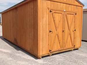 A Classic Shed - 2925 with double doors and a gable roof sits on gravel beneath a partly cloudy sky.