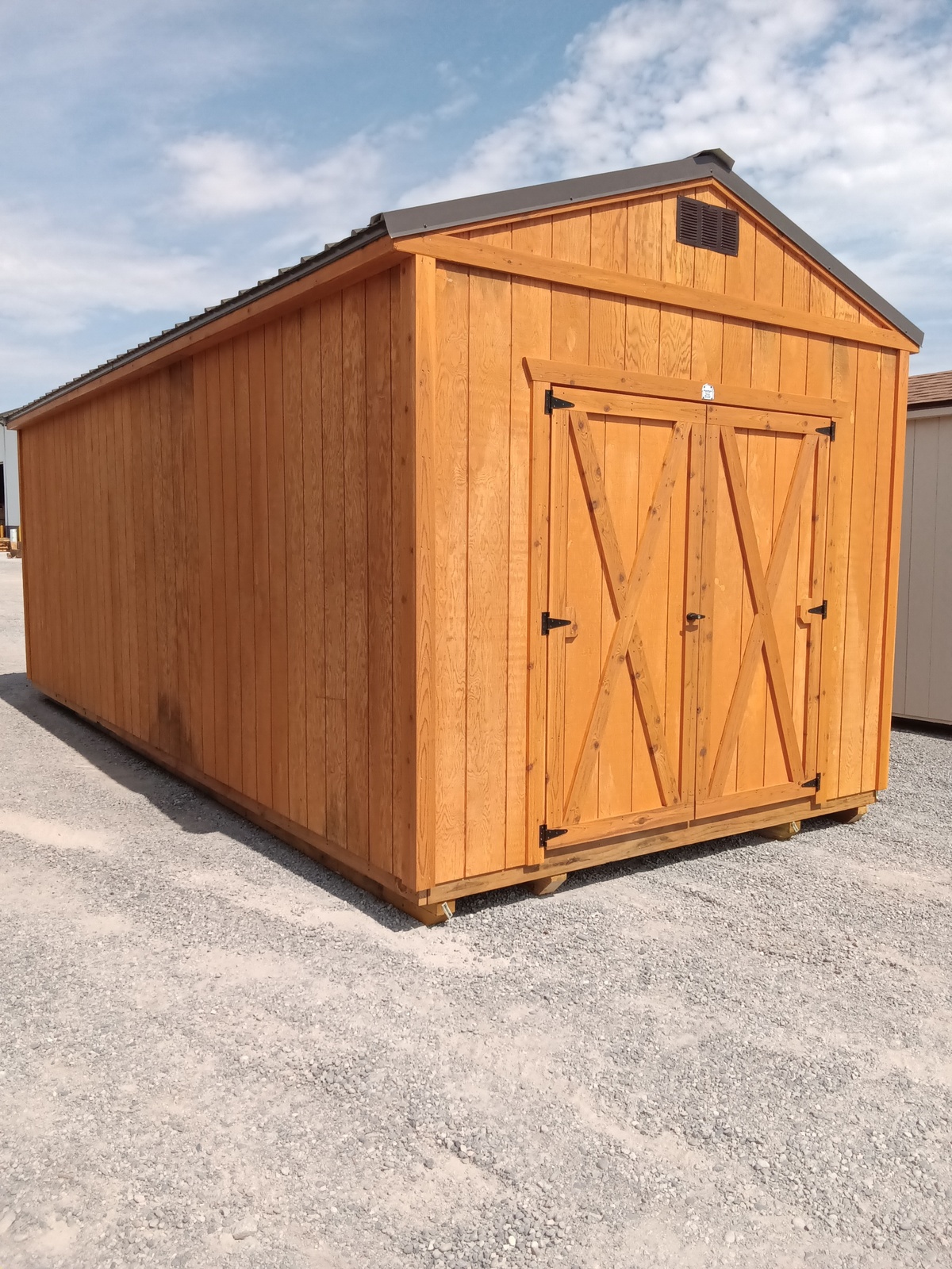 A Classic Shed - 2925 with double doors and a gable roof sits on gravel beneath a partly cloudy sky.
