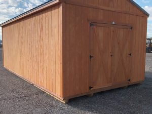 A Classic Shed - 2926 with a gabled roof and double barn-style doors is set on a gravel surface under a partly cloudy sky.