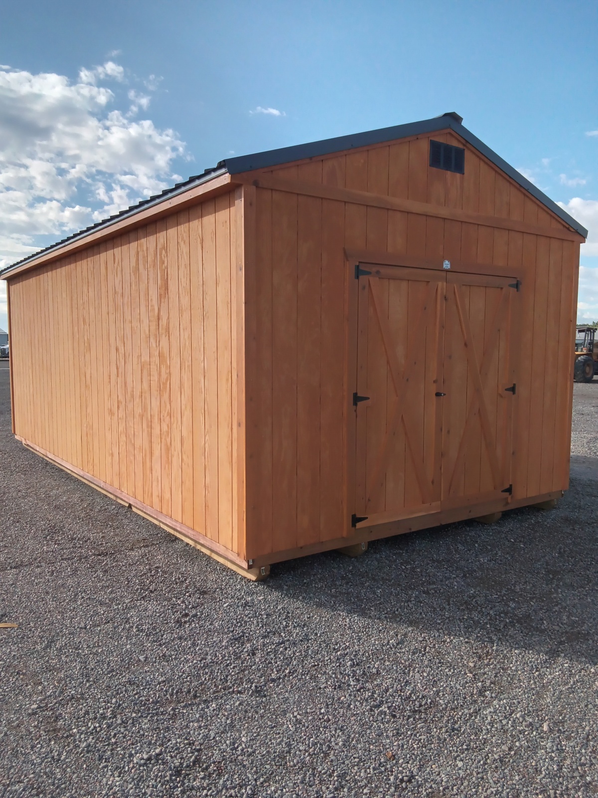 A Classic Shed - 2926 with a gabled roof and double barn-style doors is set on a gravel surface under a partly cloudy sky.